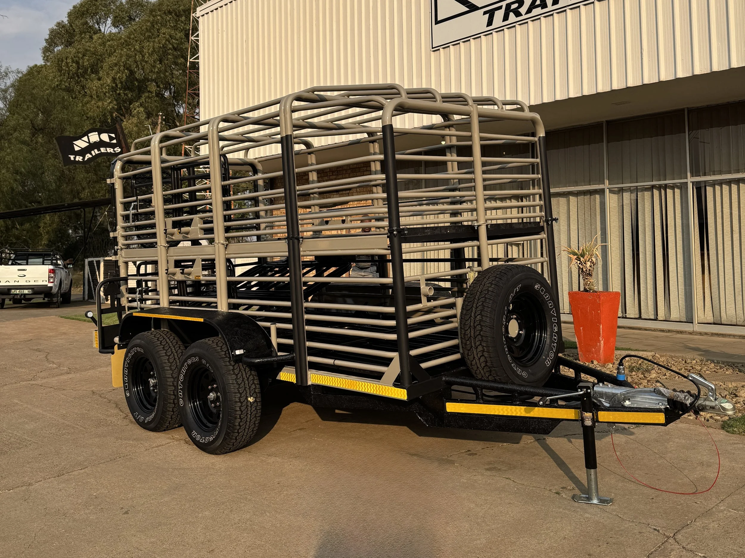 A livestock trailer with a metal frame and tires parked outside a building with a sign that reads 'TRAILERS'.