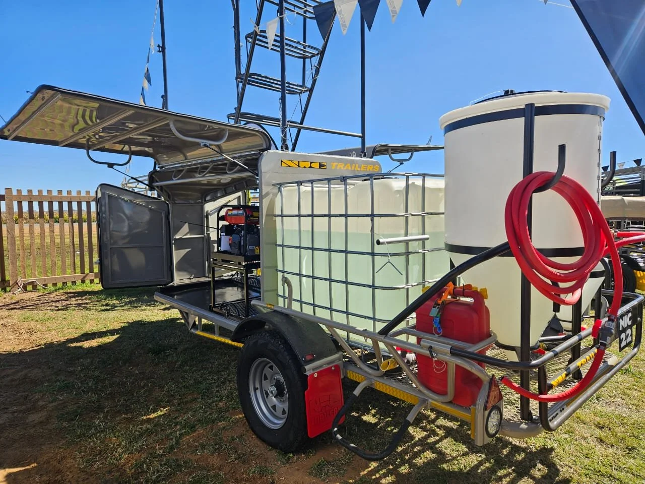 Firefighting water trailer with tanks, hoses, and equipment set up outdoors on grass under clear blue sky.