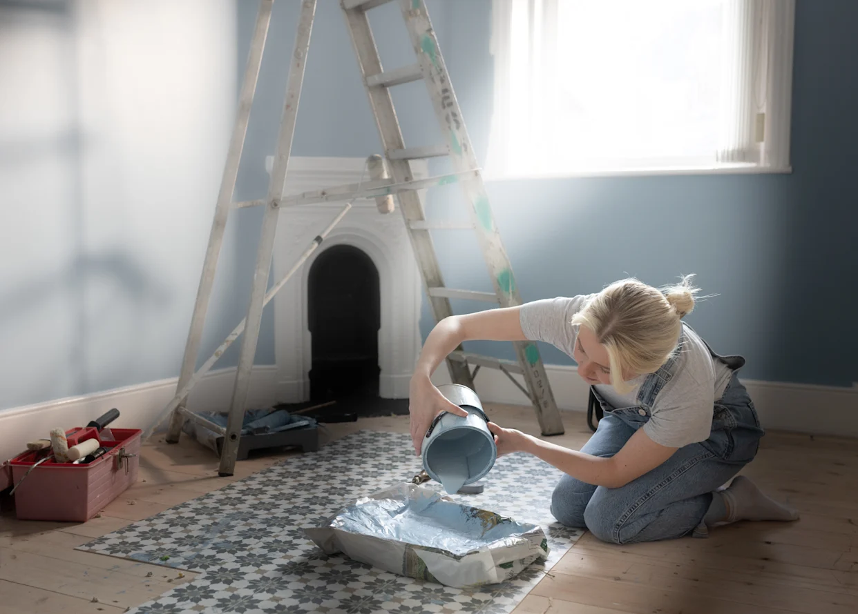 Homeowner in Howard County preparing paint in a tray for a DIY room project with ladder and supplies ready to go.