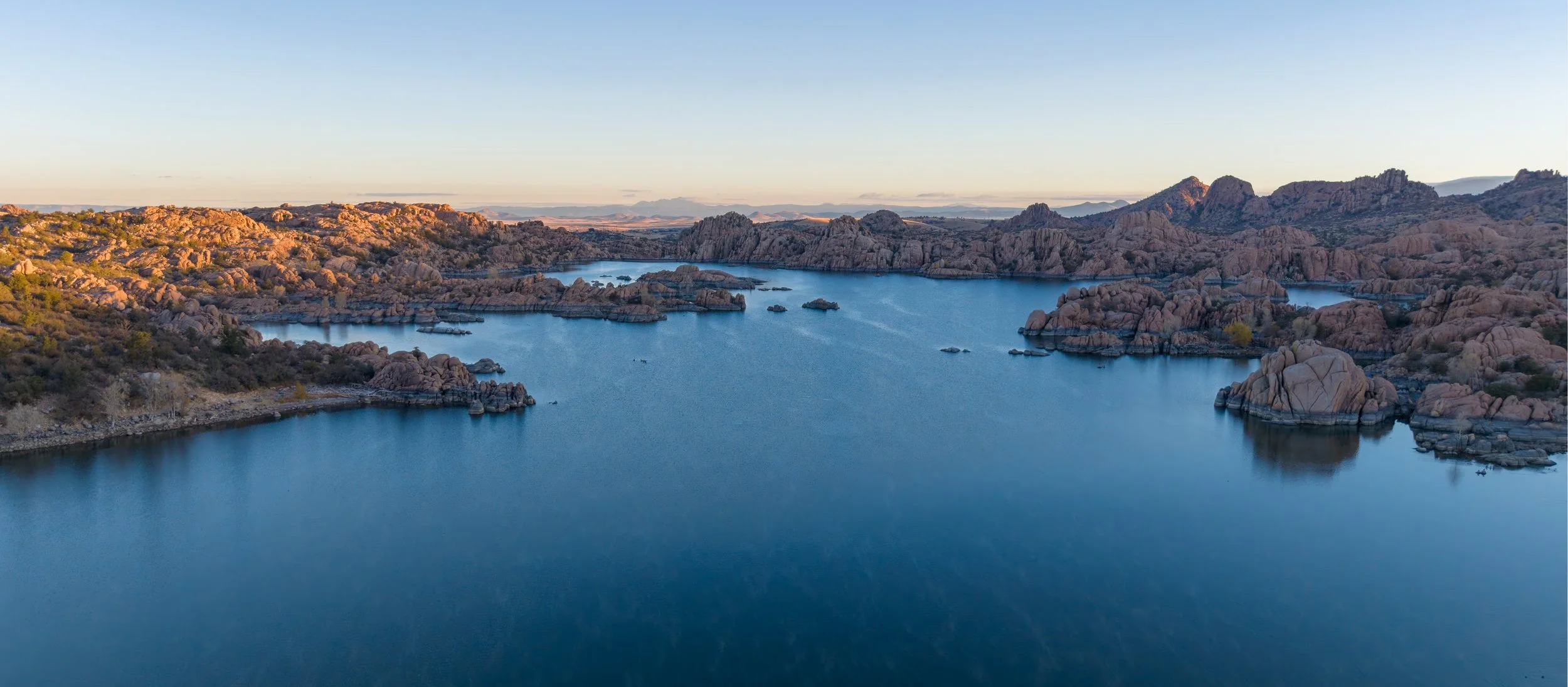 Aerial view of a desert landscape with Watson lake and rocky formations, under a clear blue sky.