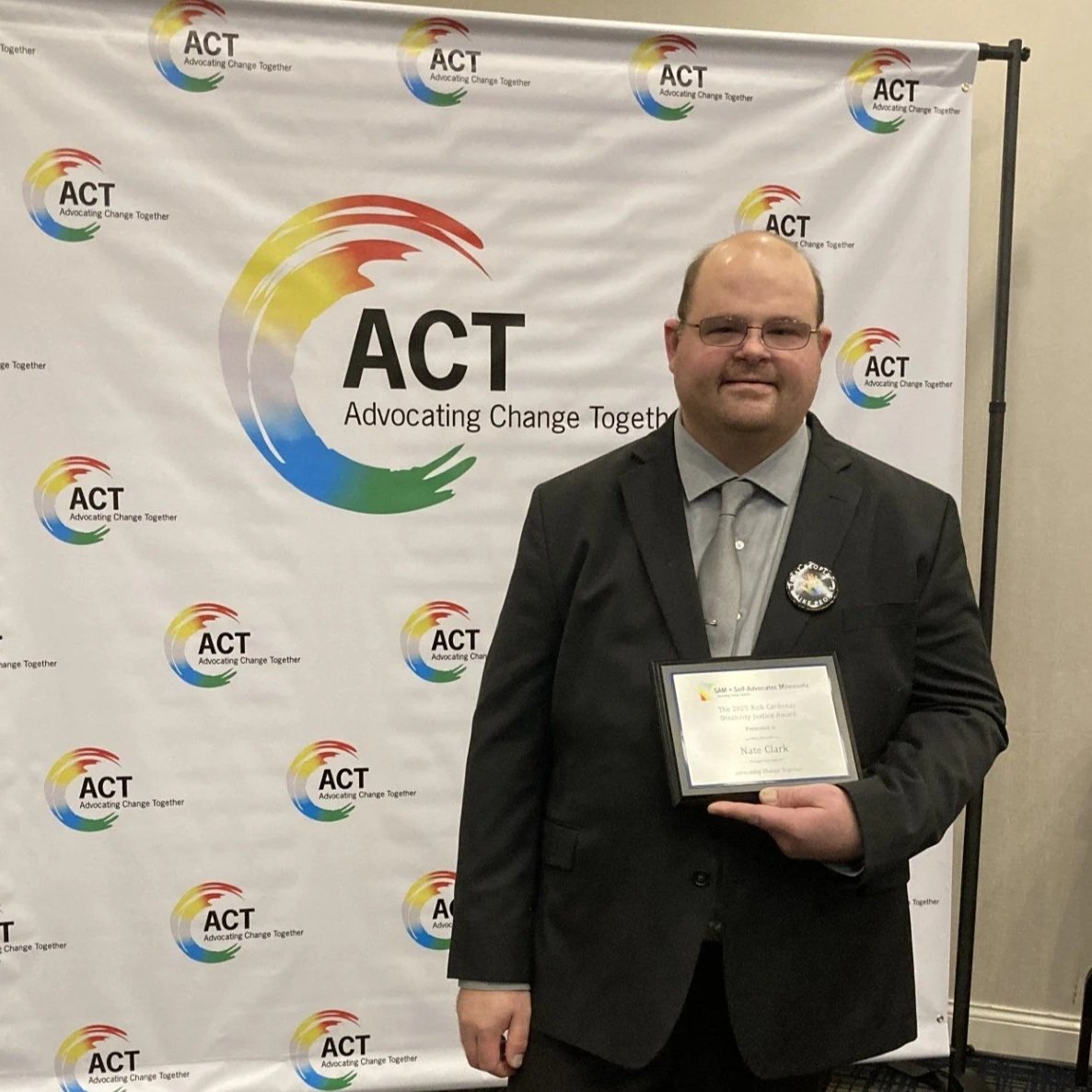 Photo of Nate Clark after wining an award at the ACT conference. He is wearing a dark suite with a grey tie.