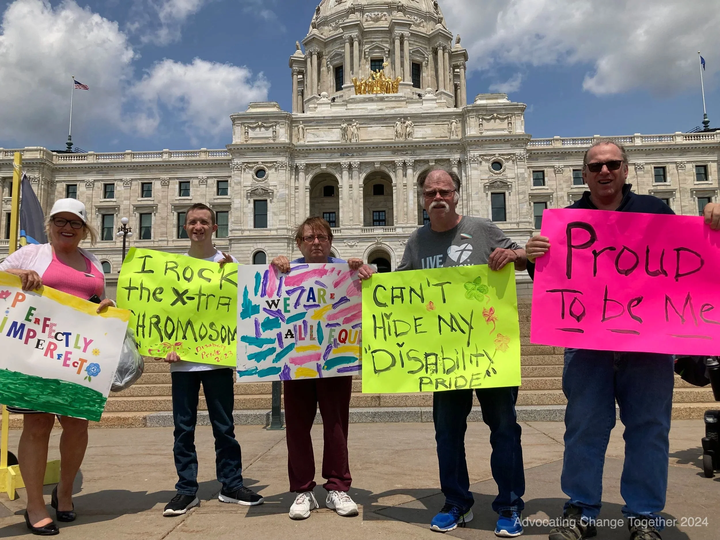 A group of five people holding signs with positive messages in front of the state capitol.