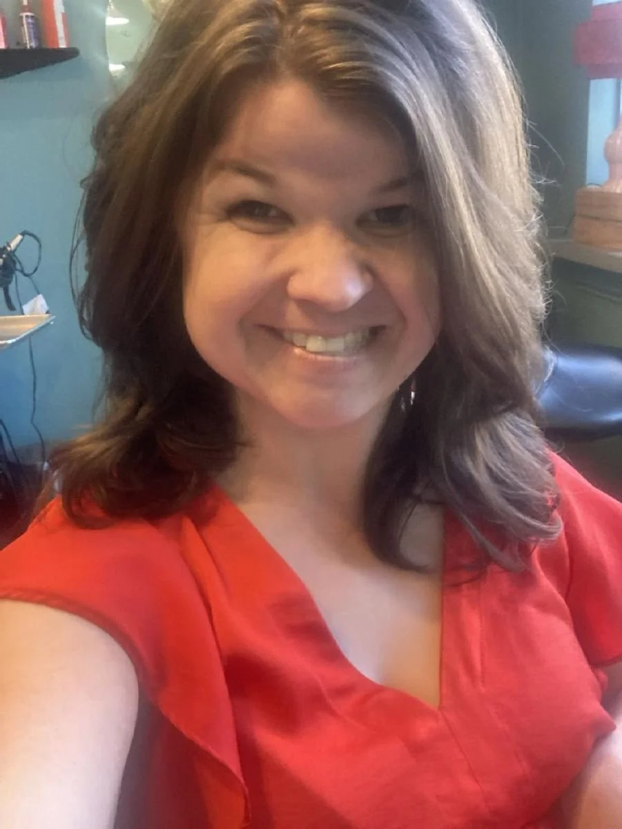 Rochelle wearing a red shirt with long brown hair. She is smiling and taking a selfie.