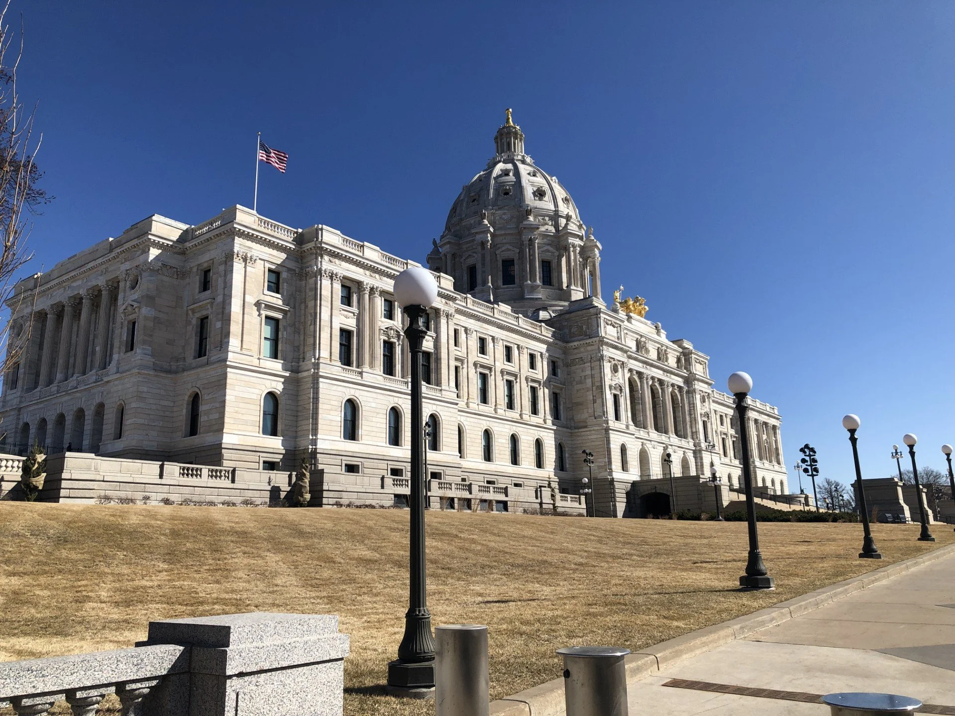 Photo of the MN state capitol. Tan grass is out front with a deep blue sky.