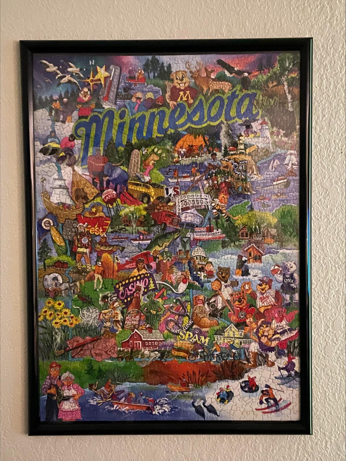 Framed completed puzzle. 'Minnesota' text top middle with many MN landmarks on the puzzle.