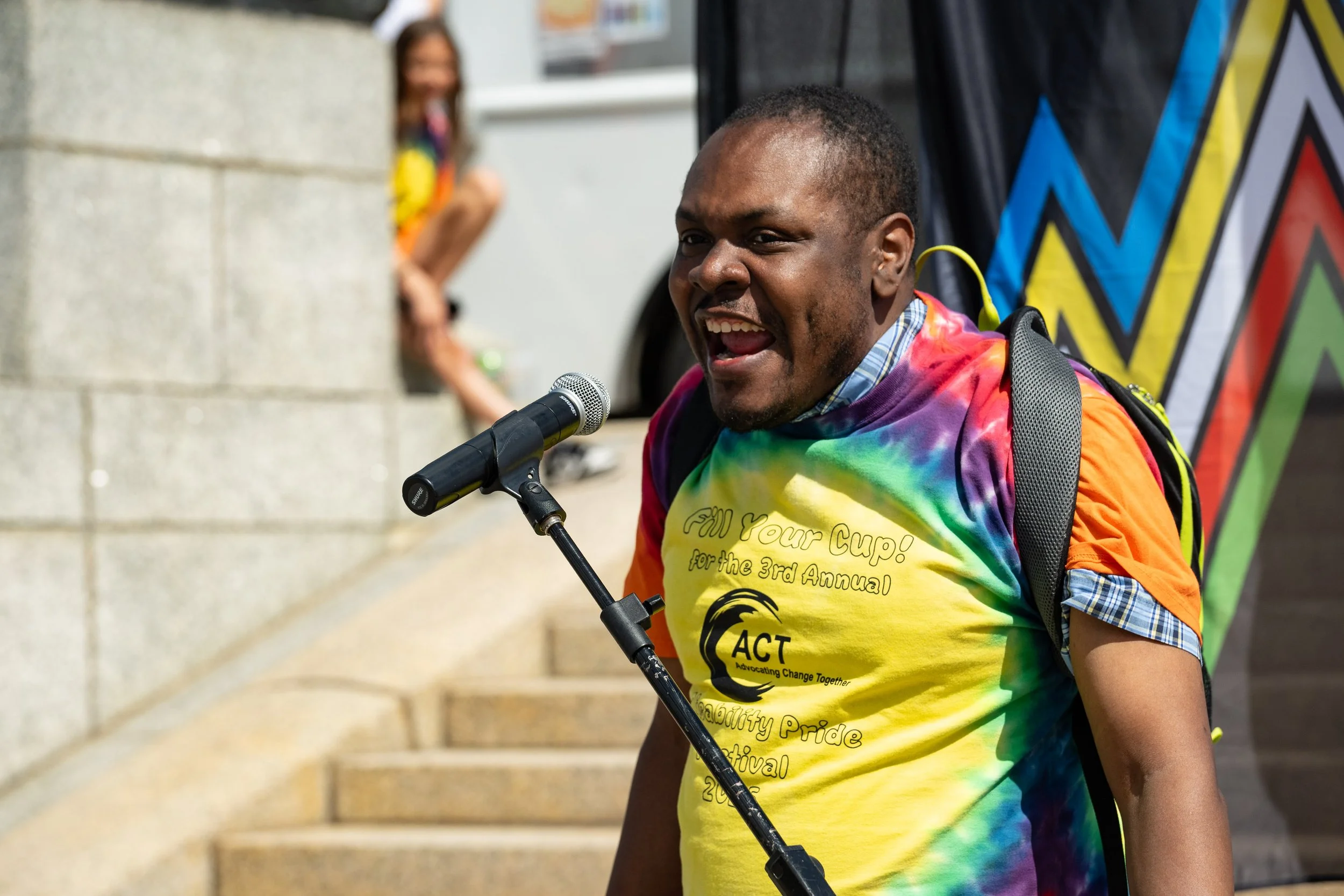 Number speaking in front of a colorful backdrop while wearing a rainbow tie-dye shirt.