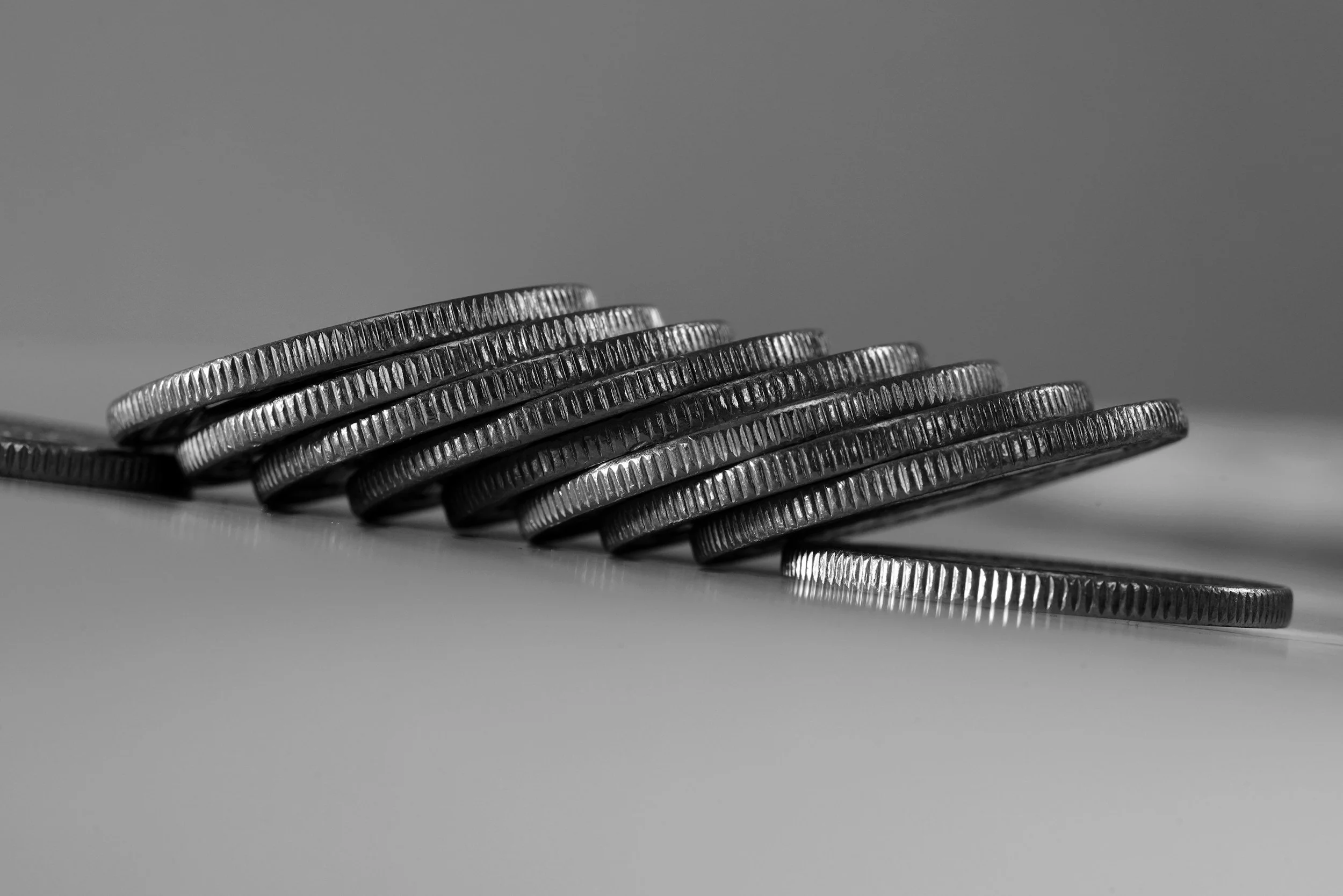 A stack of ten silver coins with ridged edges, partially tilted on a smooth surface, in black and white.