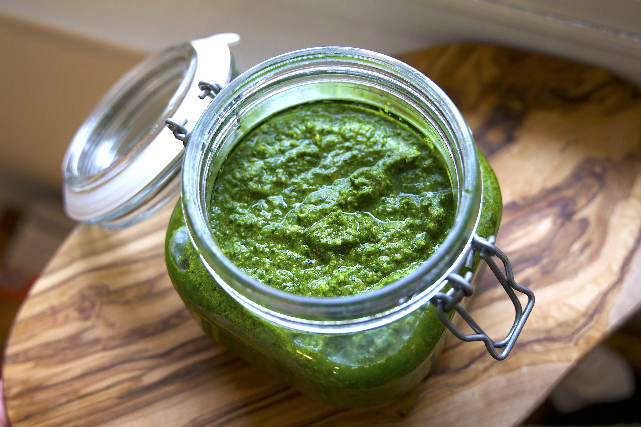 Homemade garden greens pesto in a glass jar on an olive wood cutting board