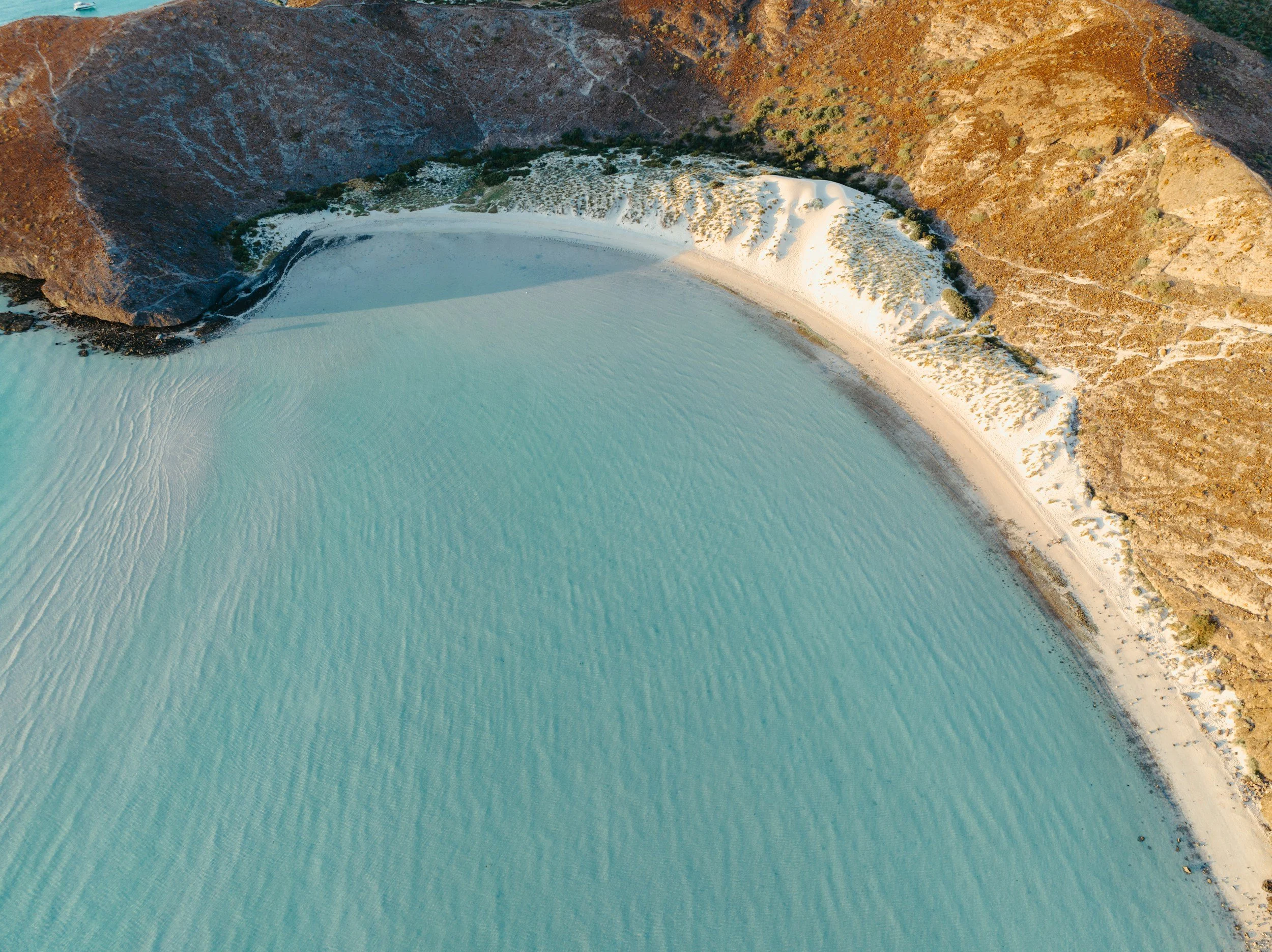 Vista aérea de un cráter volcánico con un lago de agua azul claro en el interior, rodeado por paredes rocosas y vegetación dispersa.