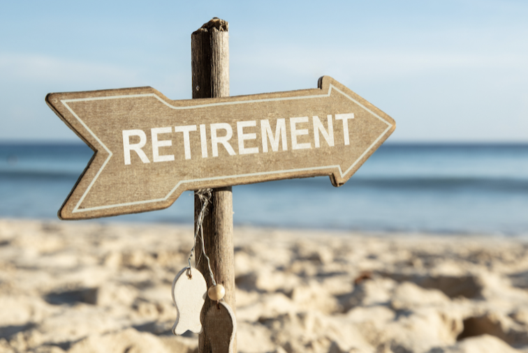 A wooden sign pointing to the right with the word 'Retirement' on a beach with sand and ocean in the background.