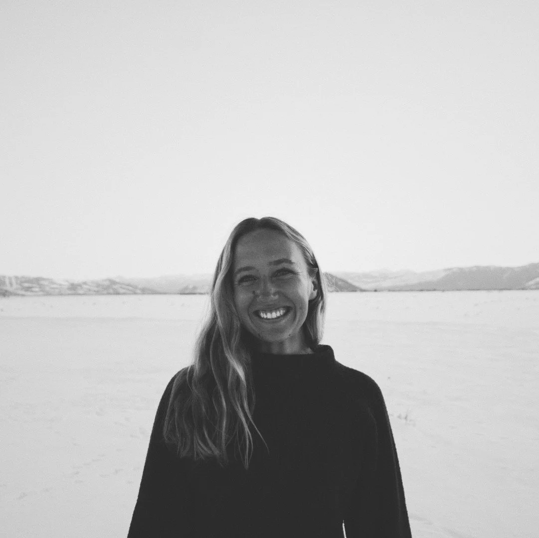 Smiling woman with long hair standing outdoors in a snowy landscape with hills in the distance