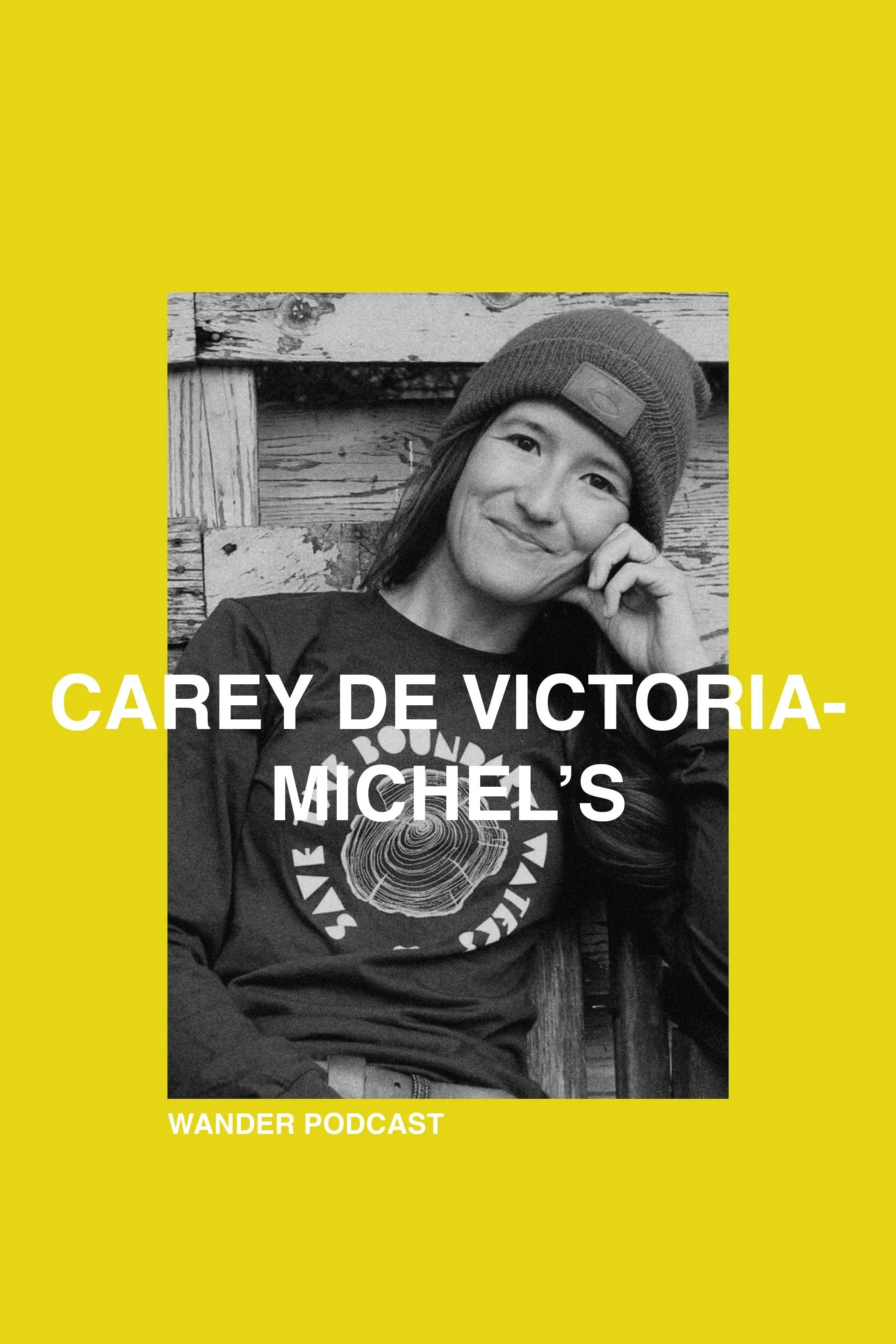 Black and white photo of a woman wearing a beanie and a graphic t-shirt, sitting in front of a wooden background, smiling with her hand resting on her cheek. Overlaid text reads 'Carey de Victoria-Michel's Wander Podcast'.