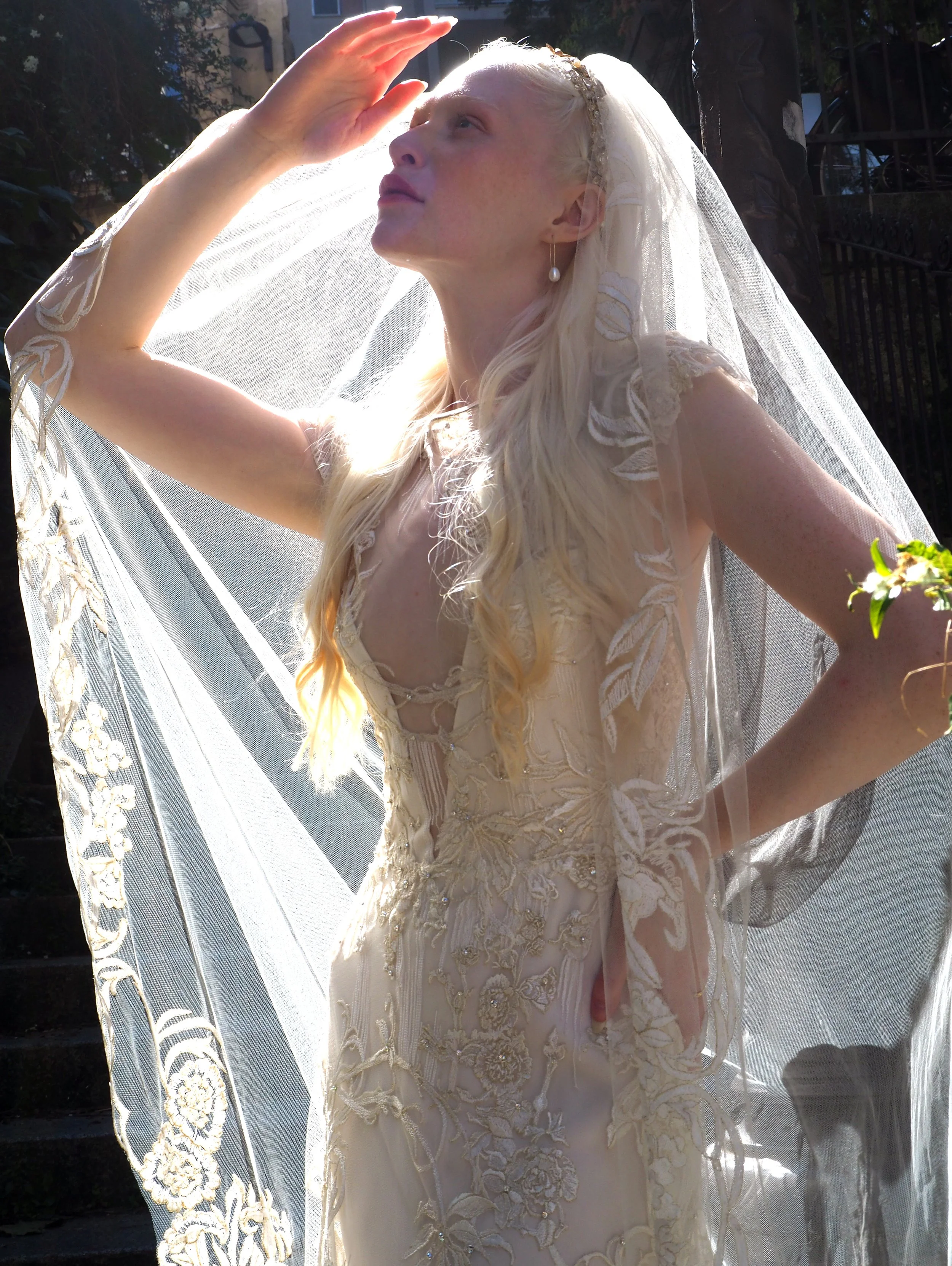 The Delilah Gown has a softly structured bodice with a deep, plunging V-neckline and a slim fitted skirt in a peach blush silk charmeuse with an Ivory silk georgette overlay. The delicate Arte Nouveau embroidered tulle from Como, Italy  is hand appli
