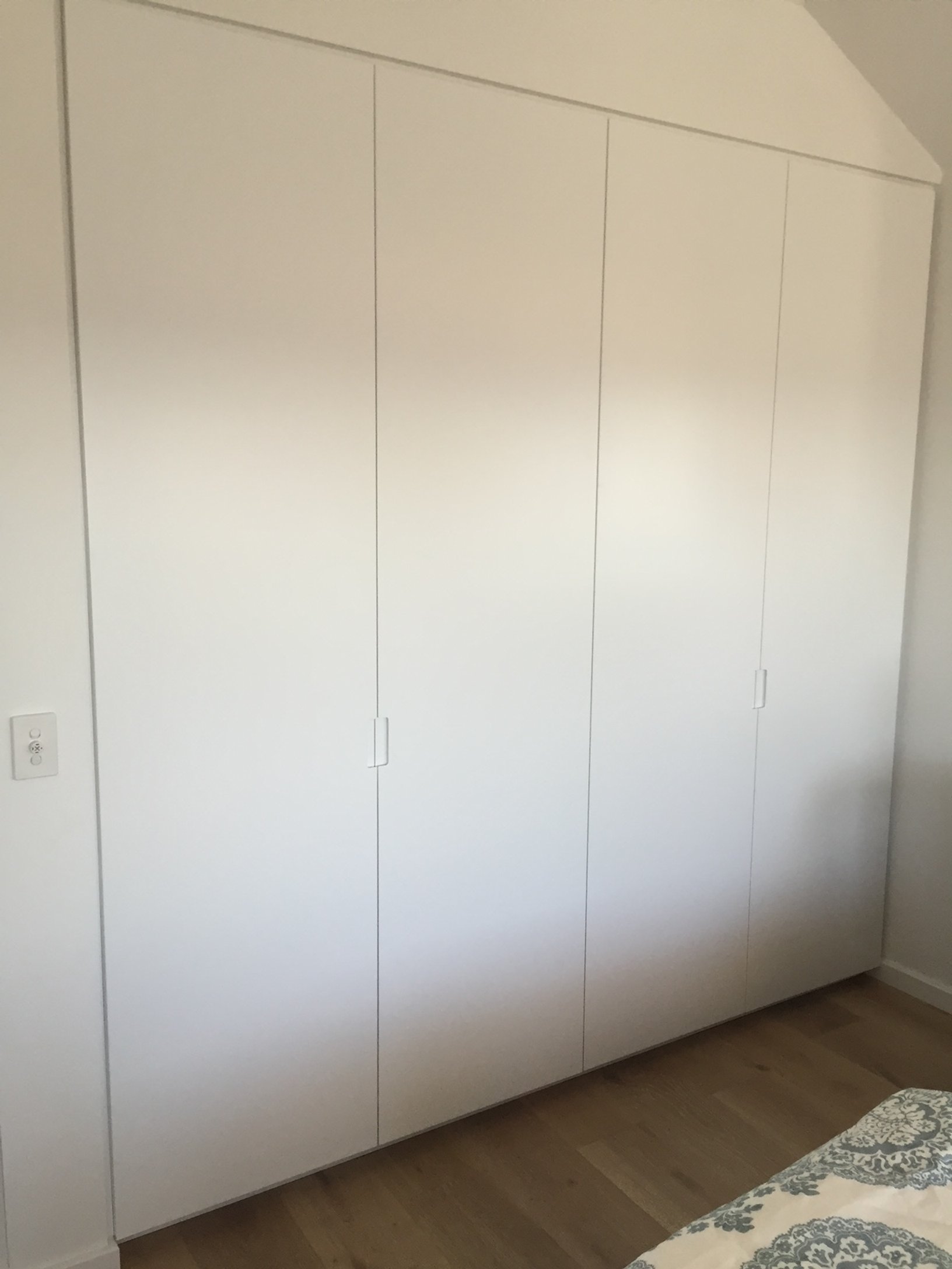 A large white wardrobe with four doors in a bedroom, with a wooden floor.