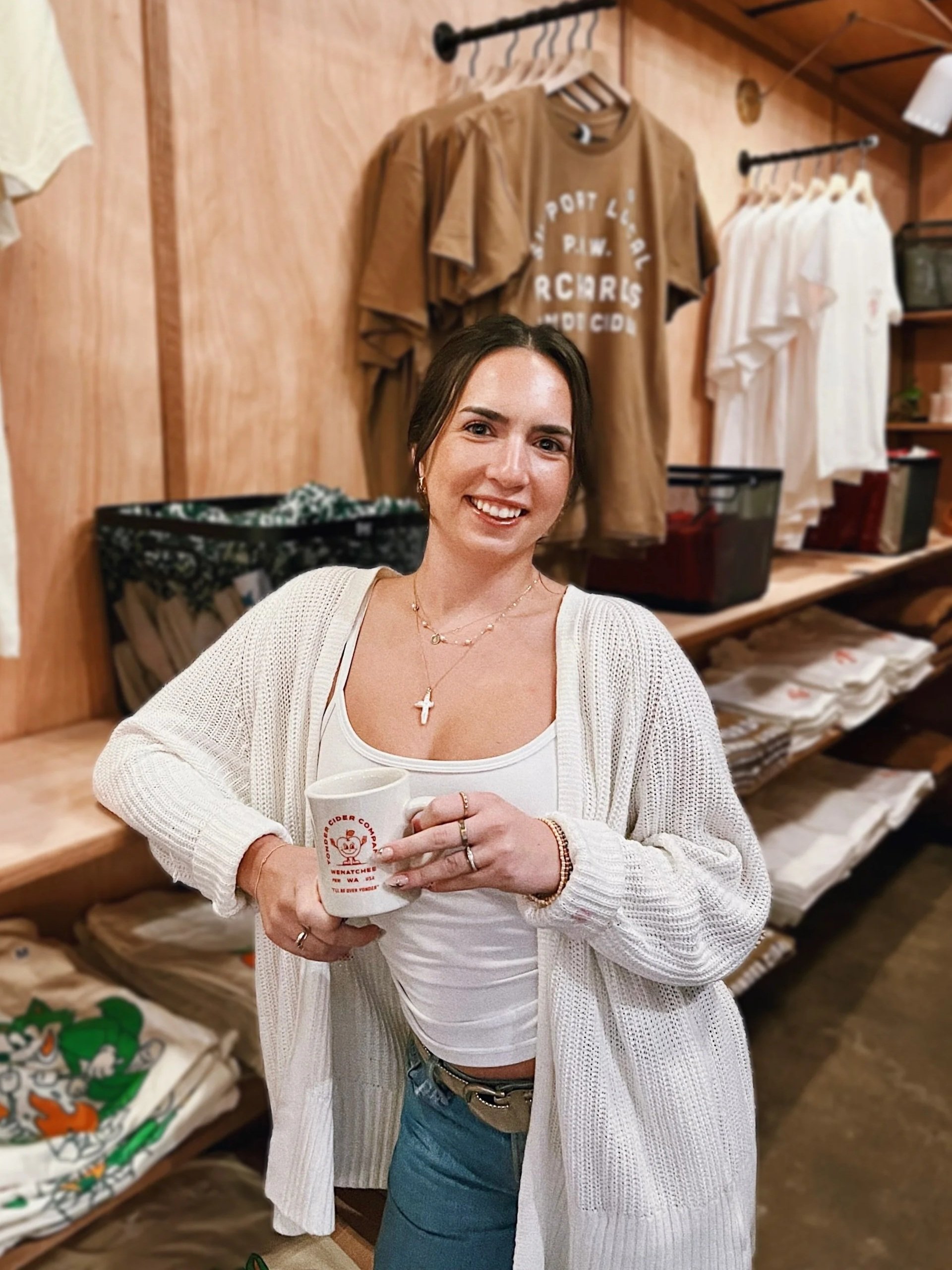 A woman smiling and holding a mug of cider in a taproom setting