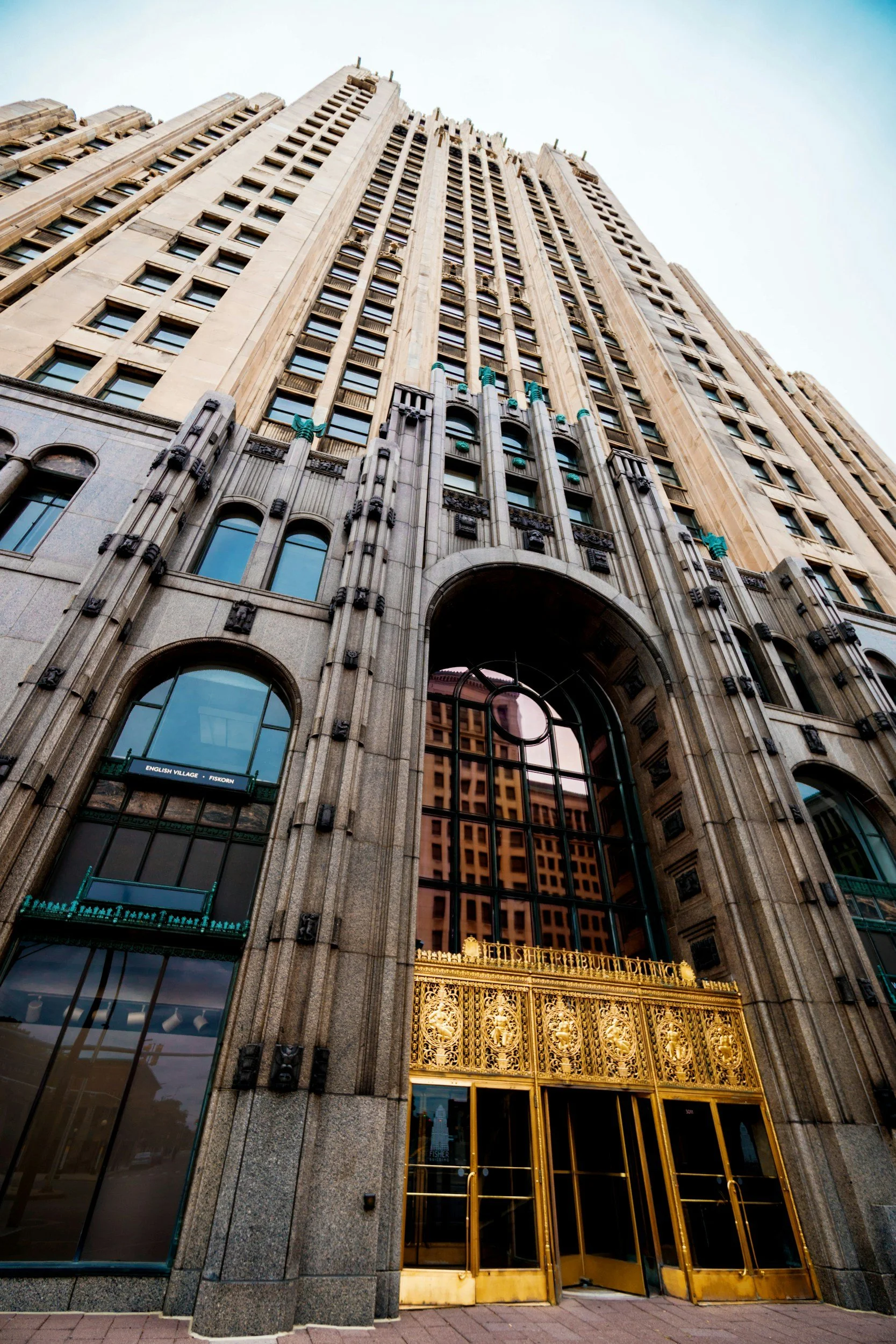 A tall historic building with an arched entrance, ornate golden gate, and multiple windows, viewed from ground level looking upward.