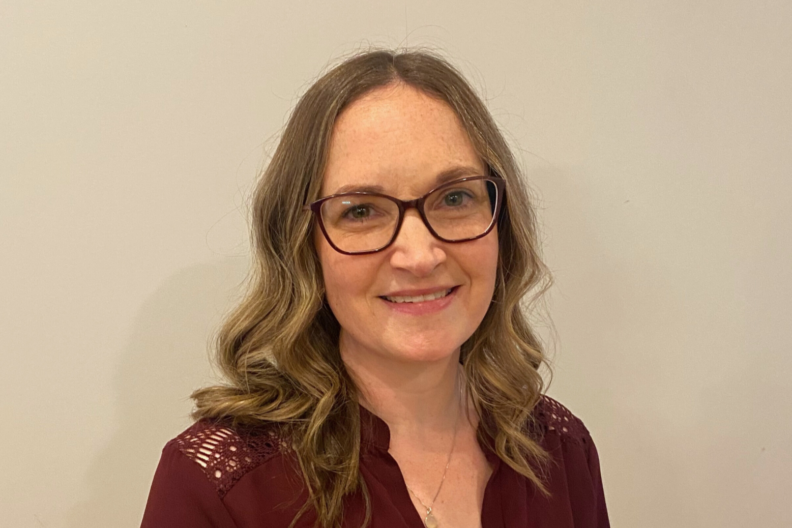 Person with lightbrown/ blonde shoulder length hair wearing glasses looking at the camera smiling. 