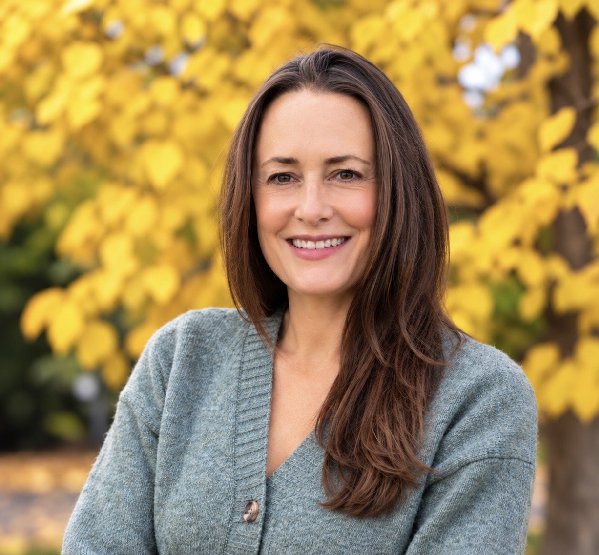 A smiling woman in front of an autumn colour tree