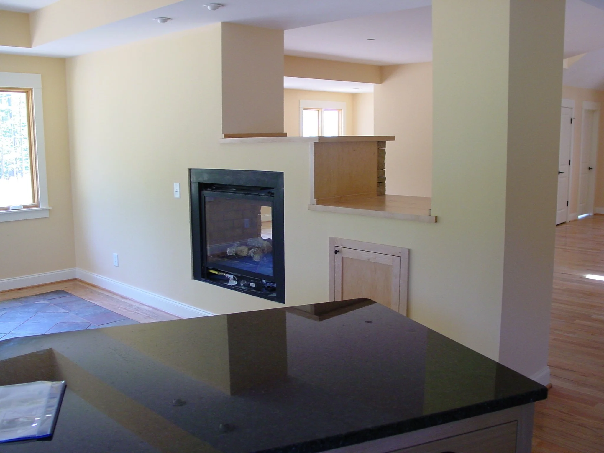 Interior view of a living area with a stone fireplace, yellow walls, and hardwood flooring, with windows letting in natural light.
