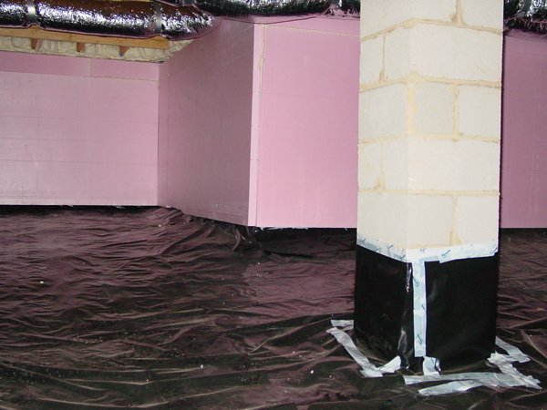 Part of a building's foundation with pink insulation foam, a brick support column covered in black waterproofing, and a black protective sheet on the ground.