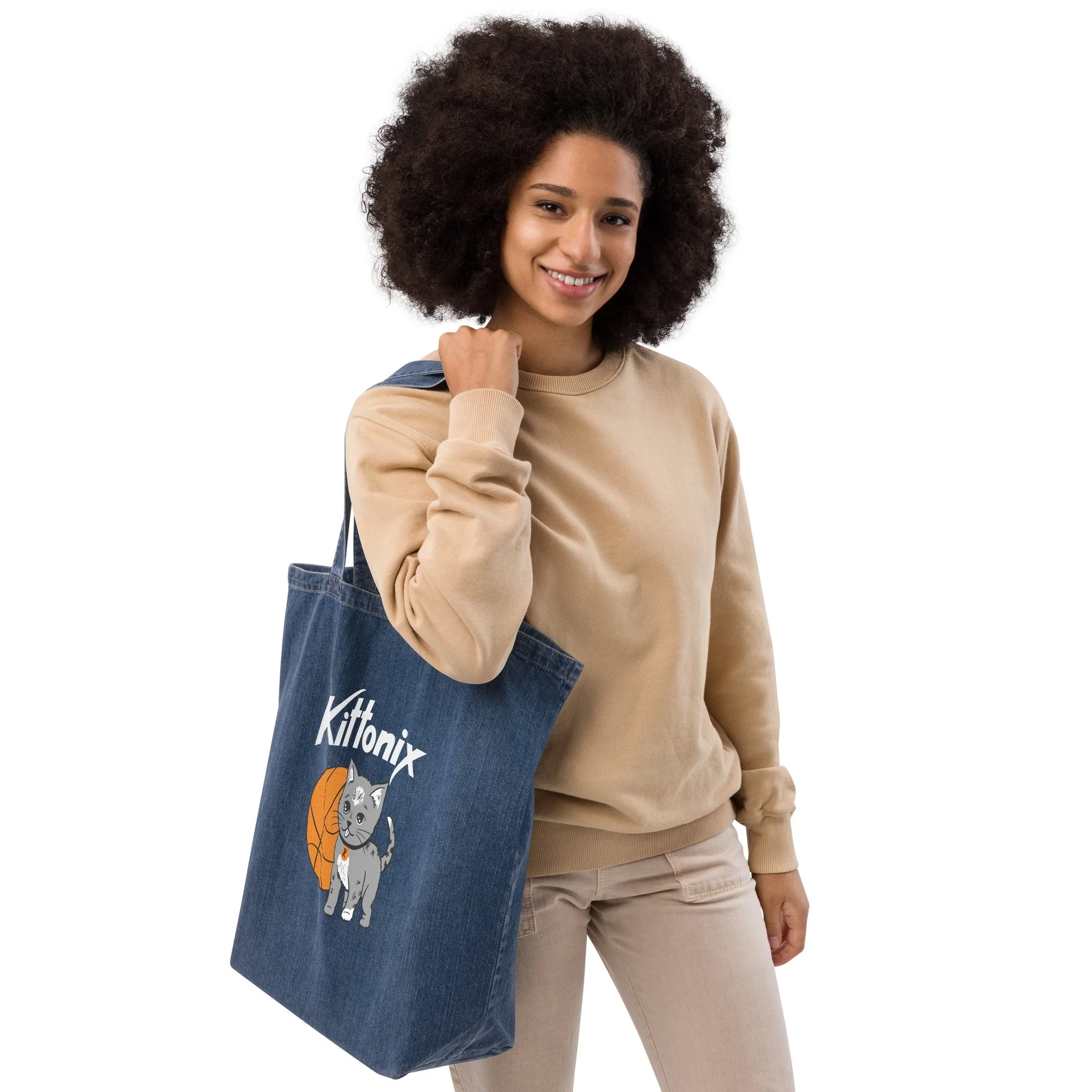 Woman holding the Kittonix denim tote bag in dark wash with original hand-drawn basketball kitten and Kittonix logo printed on front.
