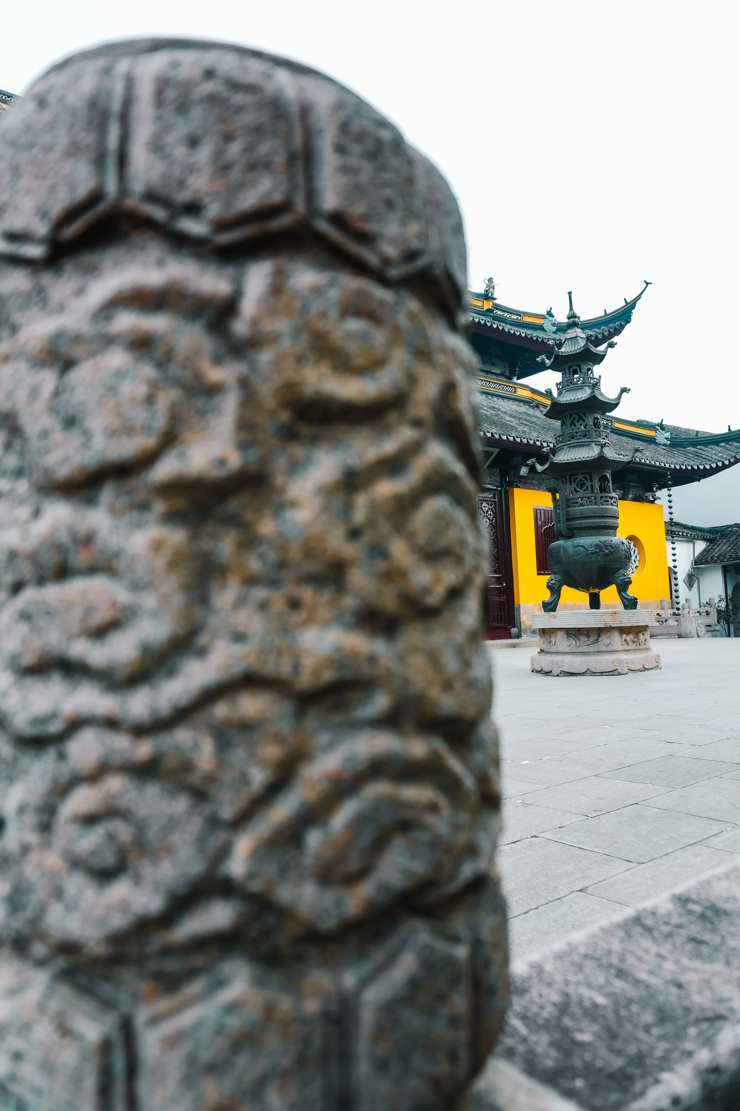 Close-up of a decorative stone carving in front of a traditional Asian temple with a large bronze incense burner and ornate roof details.