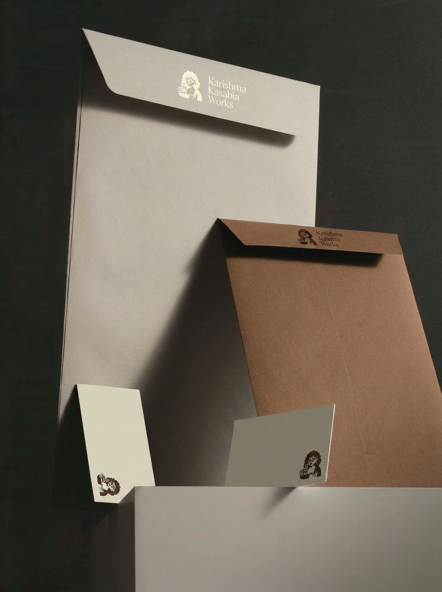 Flat lay of various paper products, including a large beige sheet, a brown envelope, and two smaller cards, all with the Karishma Kasabia Works logo featuring a woman with curly hair holding a cup.