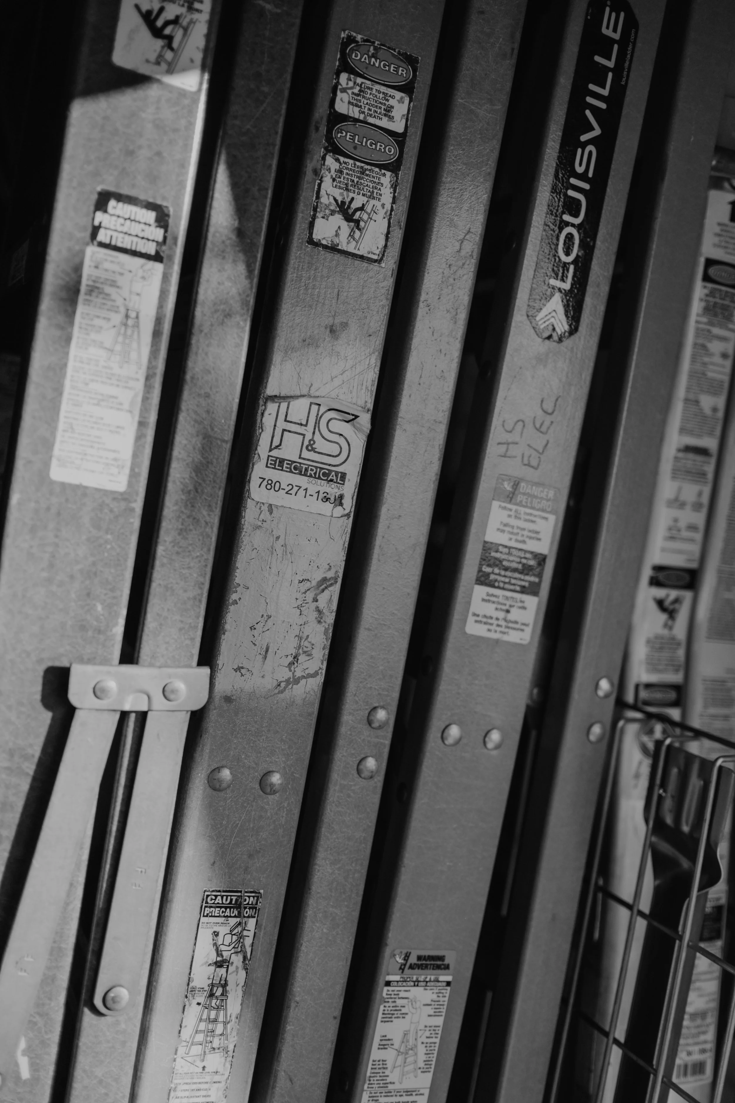 Close-up of ladder rungs with various warning and caution stickers on a metal surface.