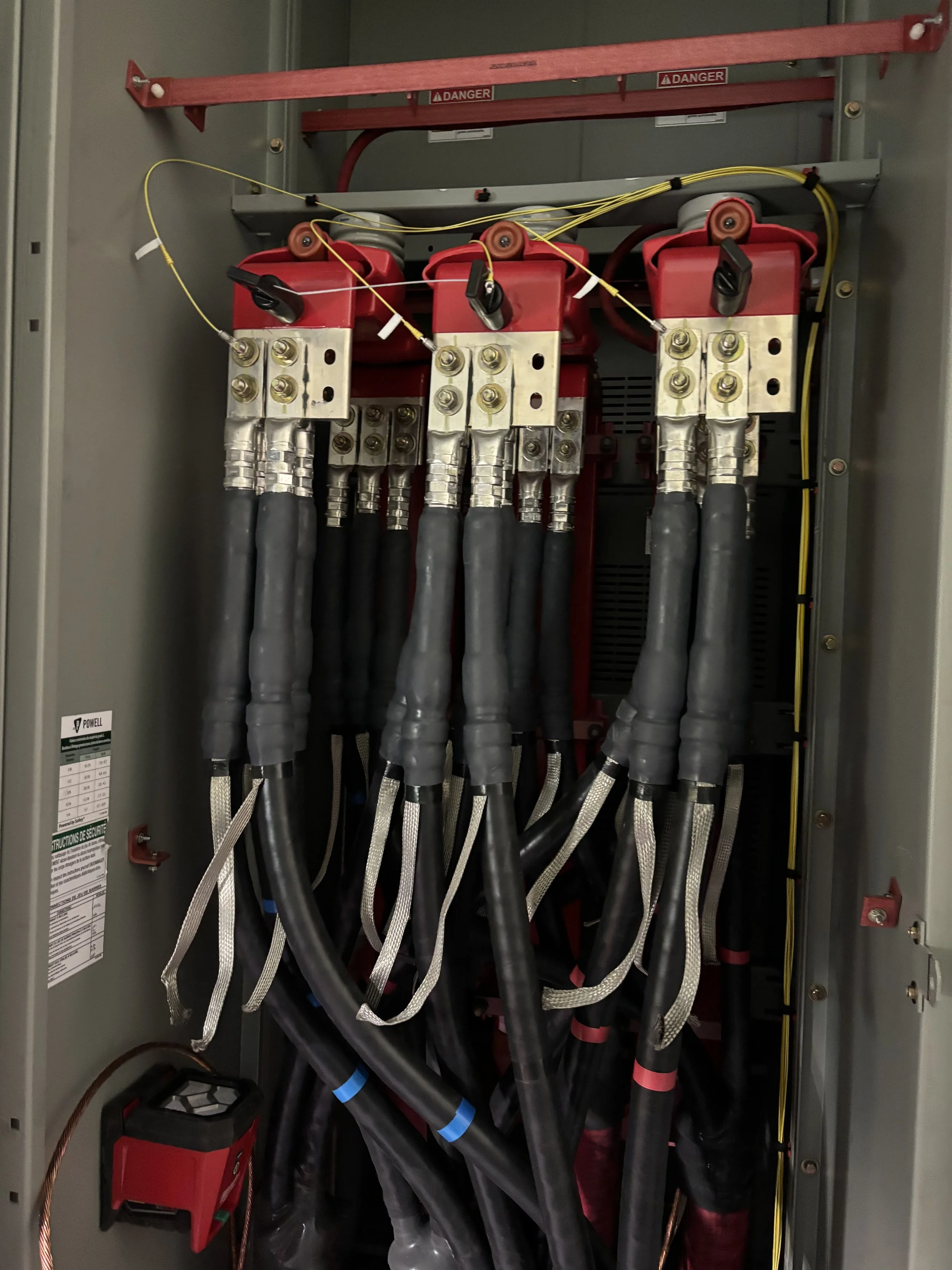 Electrical panel with large black cables connected to red circuit breakers, with warning labels and wires organized inside the box.