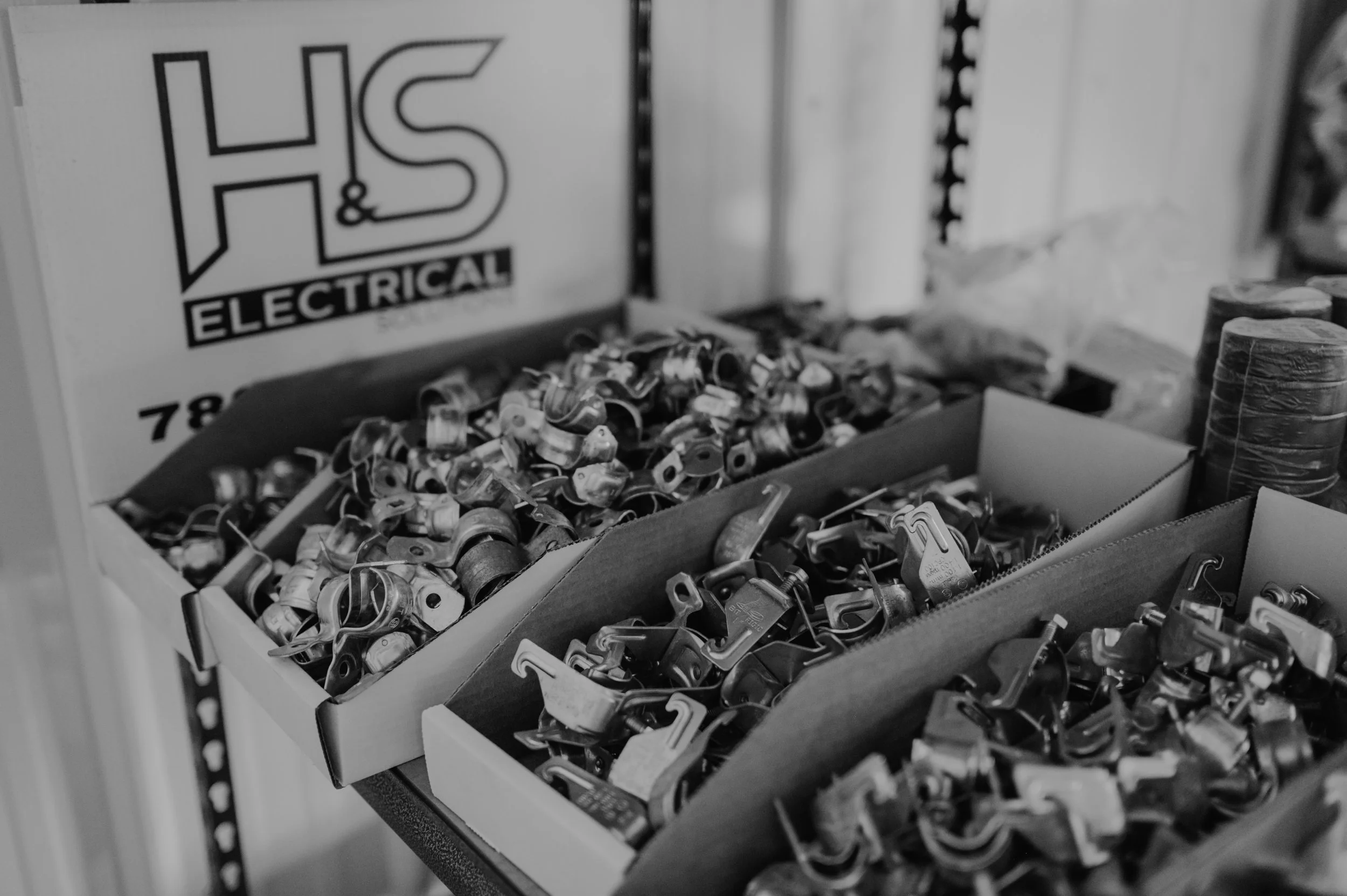 Boxes filled with small metallic electrical components on a table at an electrical supply store.