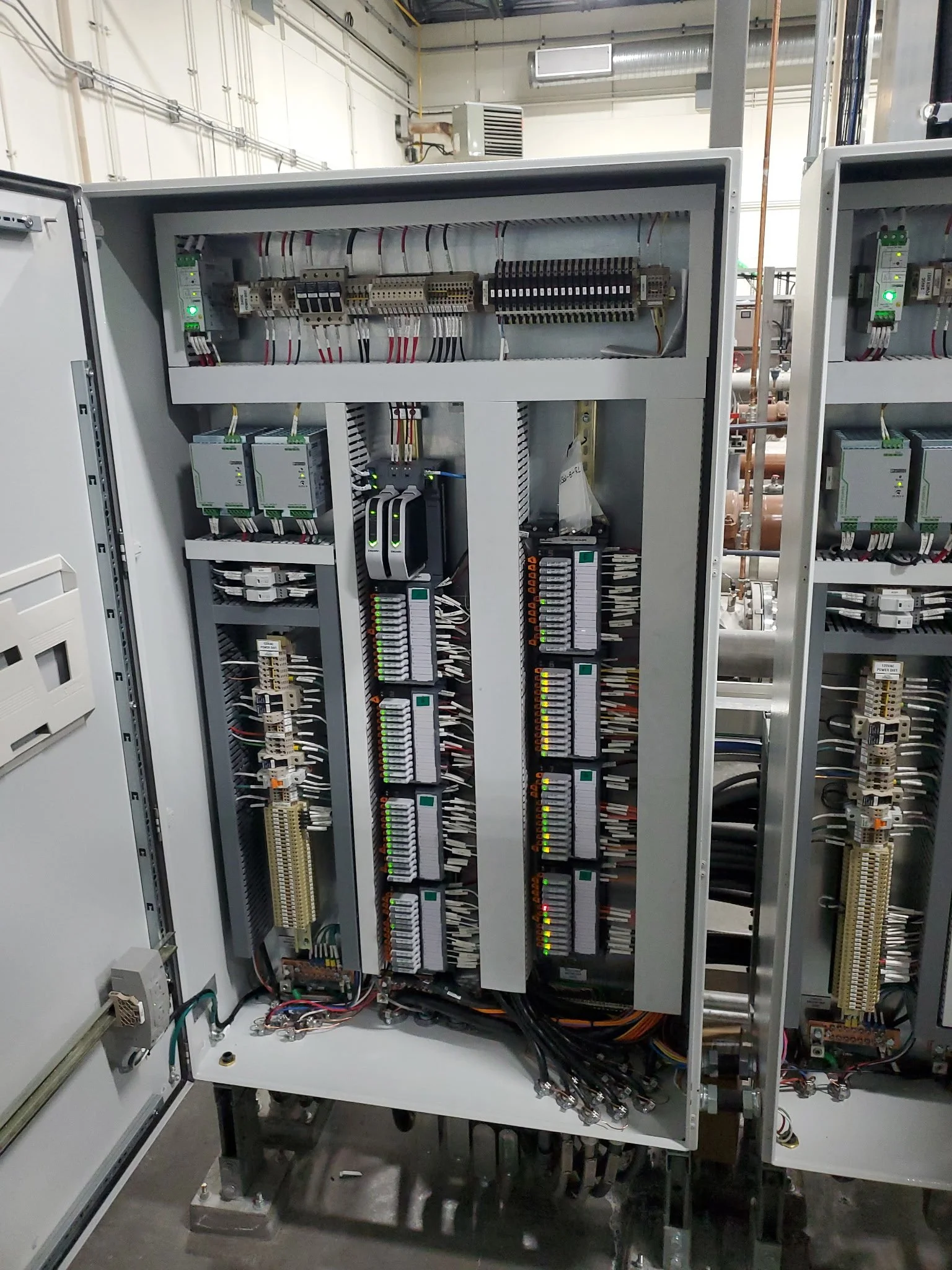 Electrical control panel with various circuit boards, wiring, and indicator lights inside an industrial setting.