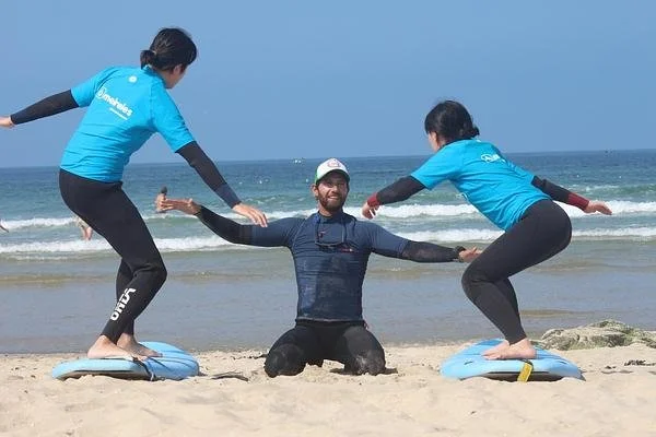 Surf Instructor in Porto Teaching Balance Techniques to Two Students on the Beach.