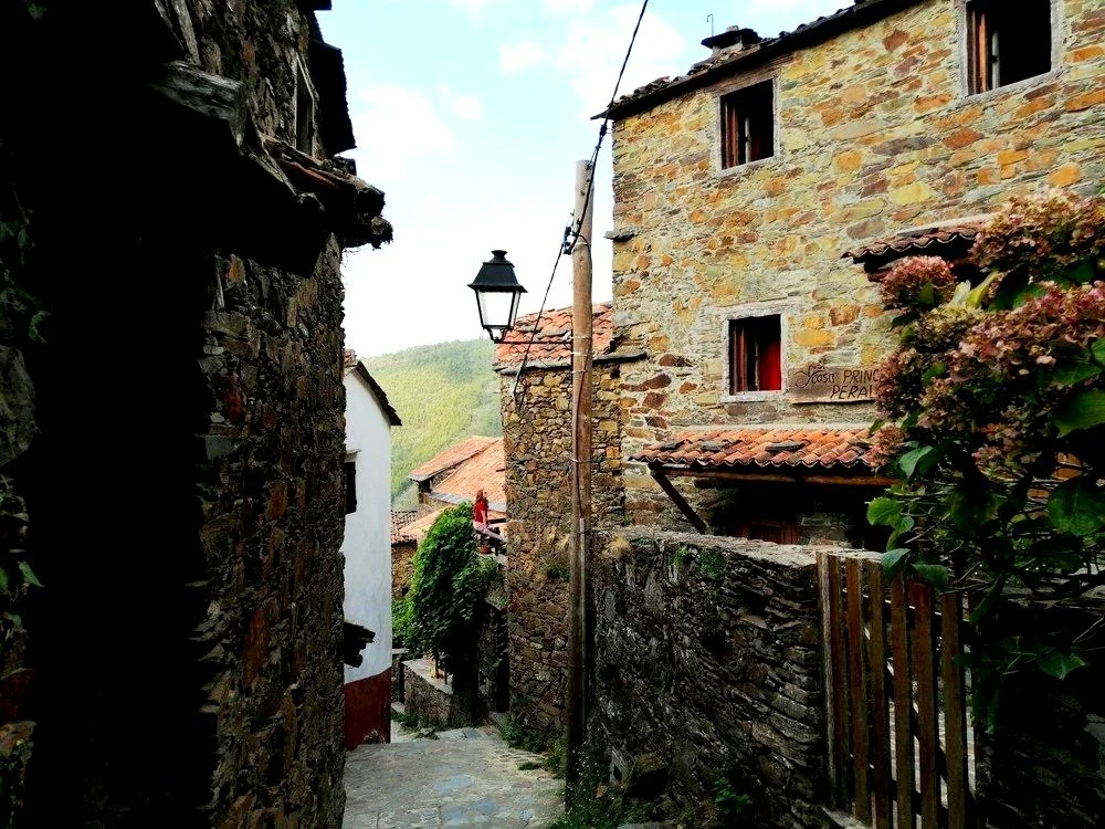 Charming narrow stone street in the rustic Schist village of Lousã Mountain, Portugal, lined with traditional stone buildings and a vintage lamp post.