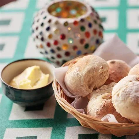 Pizzeria Pão d’Alho Ericeira: Basket of Fresh Bread Rolls with Butter and Decorative Candle Holder on a Patterned Tablecloth
