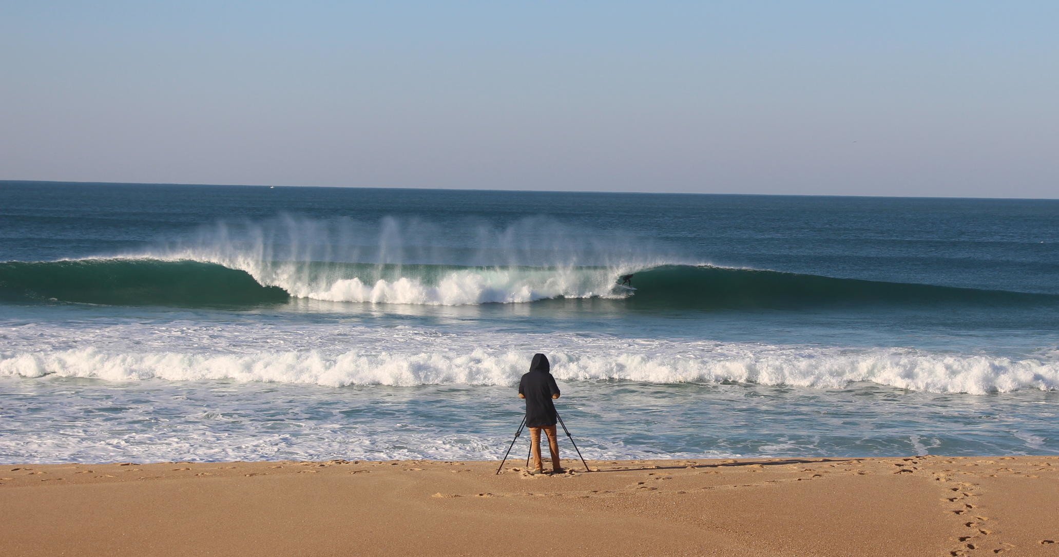 A photographer capturing the iconic waves of Portugal on the sandy beach, perfect for surf enthusiasts and coastal photography.