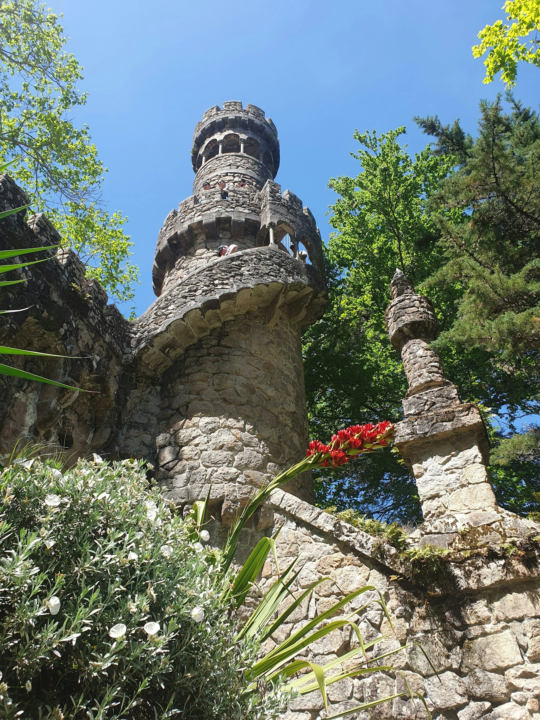 Stone tower in the gardens of Quinta da Regaleira surrounded by lush greenery and trees in Sintra