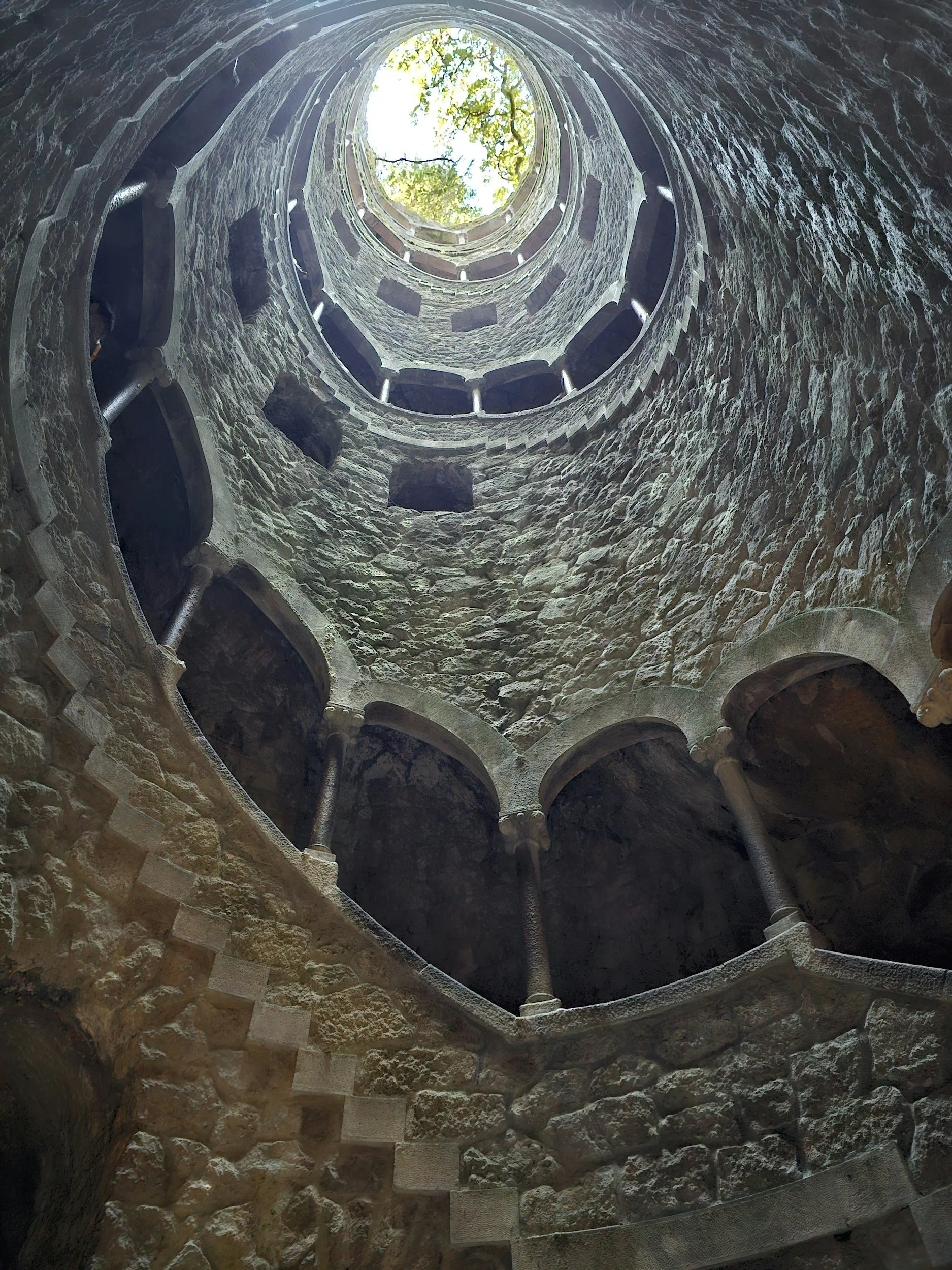 Initiation Well at Quinta da Regaleira in Sintra with spiral stone staircase descending into a moss-covered shaft