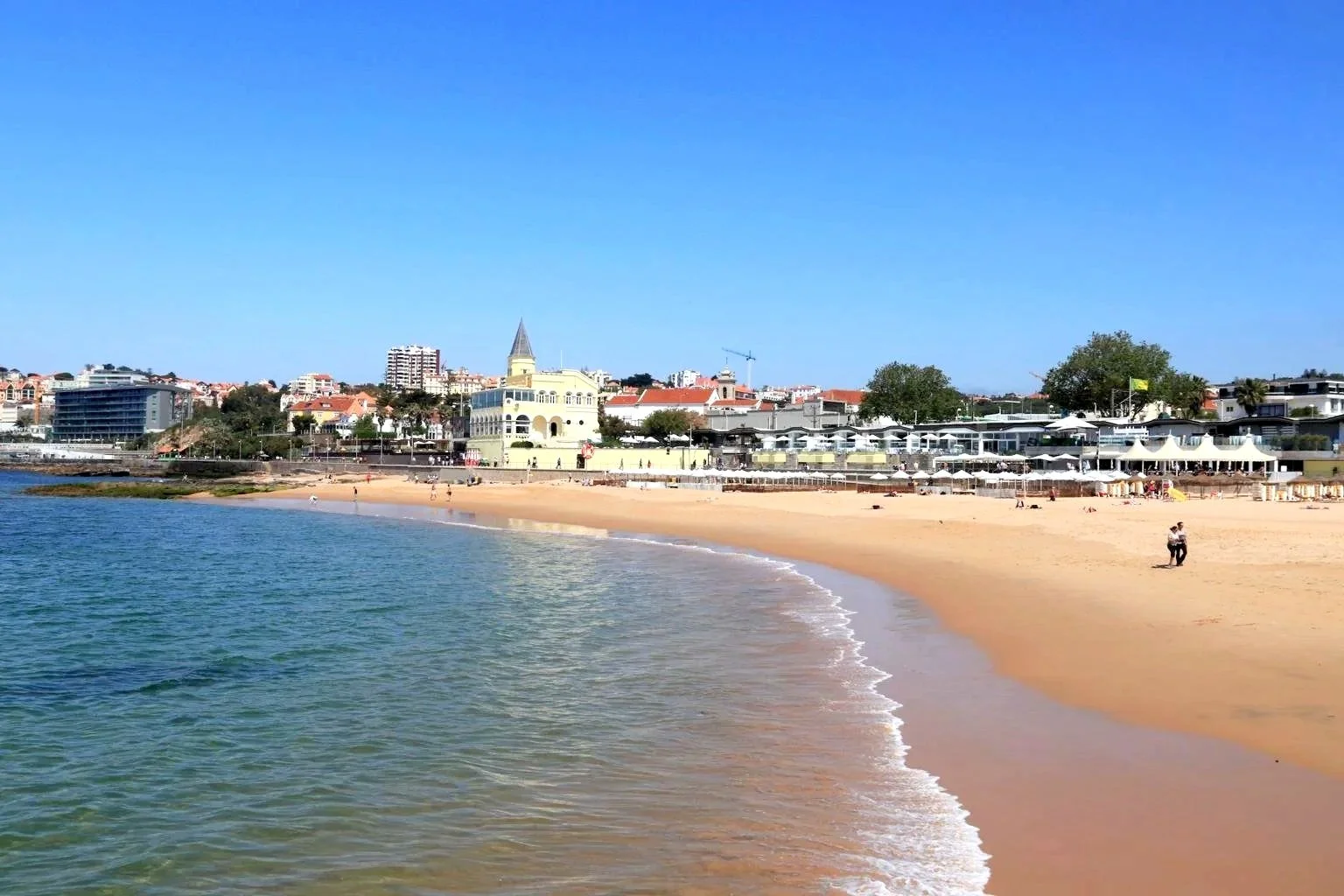 Praia da Tamariz Beach in Estoril showing sandy shoreline, beachgoers, and oceanfront promenade with historic buildings