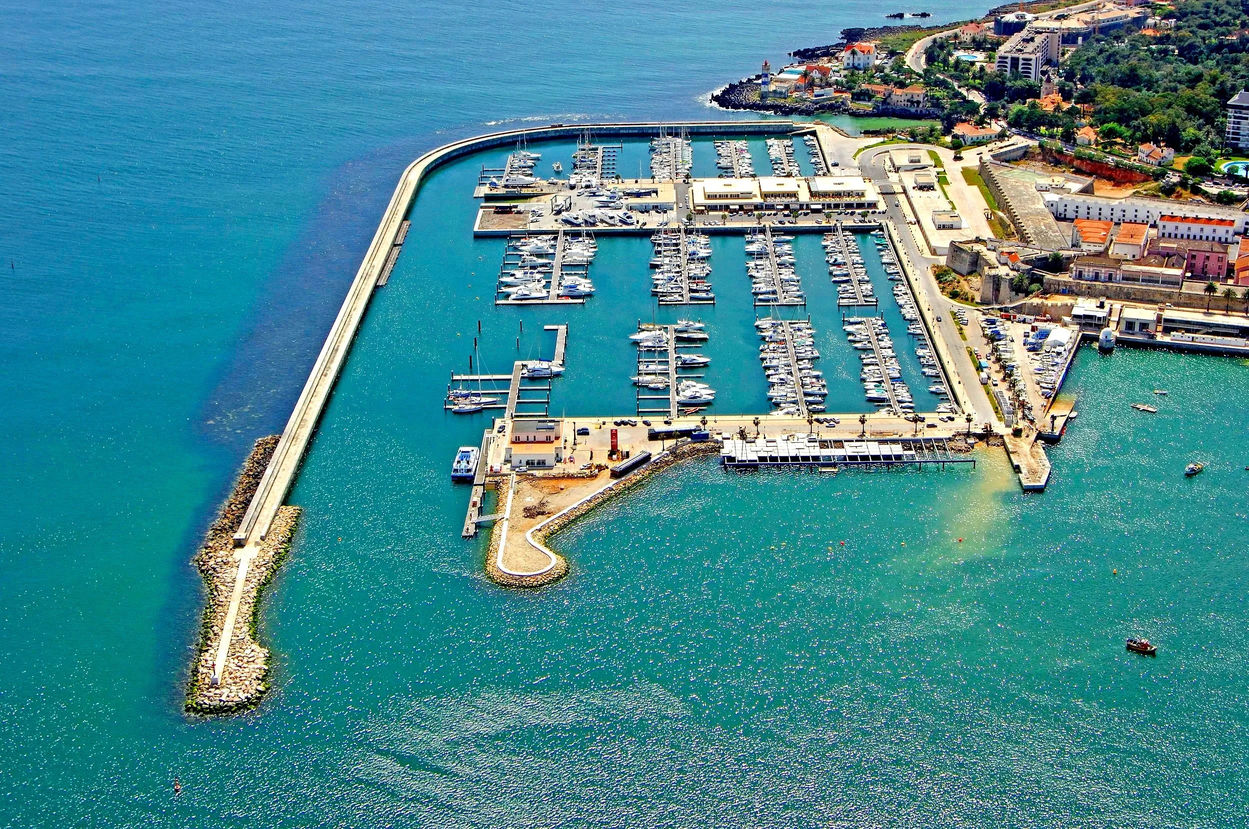 Aerial drone view of Cascais marina showing blue calm water with moored boats and coastal infrastructure