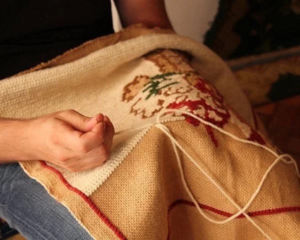 Hands stitching a beige Arraiolos rug with traditional pattern
