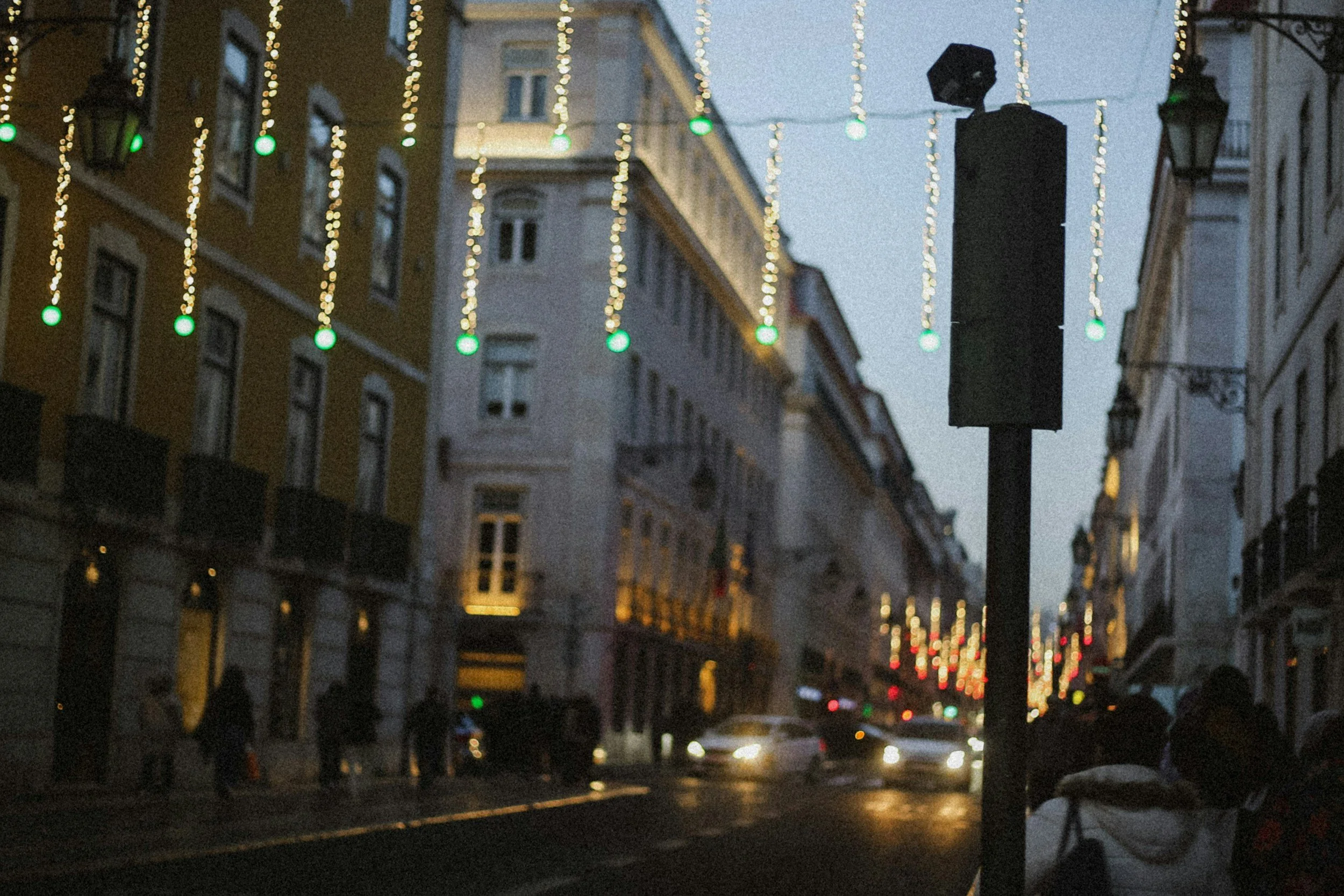 Festive Christmas lights illuminate a street near Praça da Figueira in Lisbon, creating a magical holiday atmosphere as visitors stroll toward the Tagus River.
