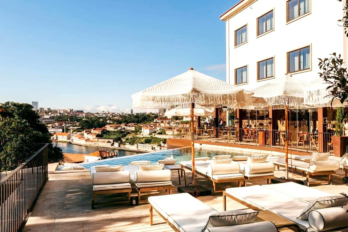 Outdoor seating area at Torel Avantgarde Porto with poolside loungers, umbrellas, and a scenic view of the cityscape and river under a clear blue sky.