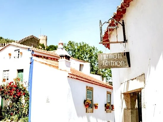 Ja!mon Ja!mon Restaurant, Óbidos: Street Scene with White Buildings, and Óbidos Castle in the Background of the Sunny Historic Town.
