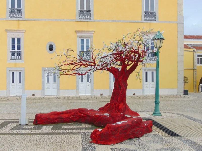 Red tree artwork displayed outside a yellow building in Cascais, Portugal, showcasing vibrant colors and artistic design.