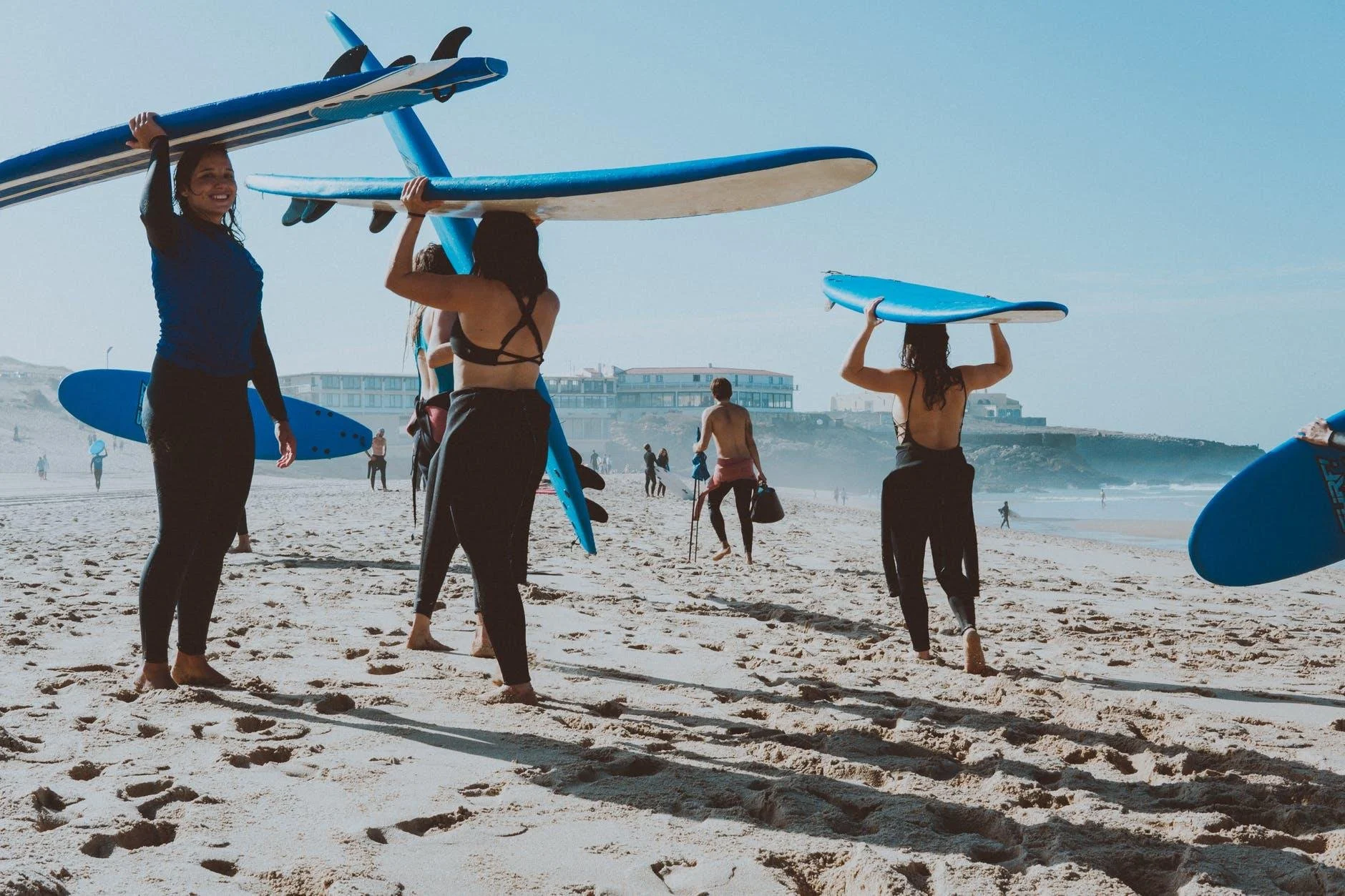 Surfers carrying blue surfboards towards a surf lesson on the golden sand beaches of Cascais, Portugal.