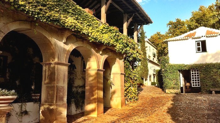 Historic building at Quinta da Pacheca - The Wine House Hotel in the Douro Valley, featuring arched stone columns, ivy-covered walls, and adjacent to a cobblestone courtyard.