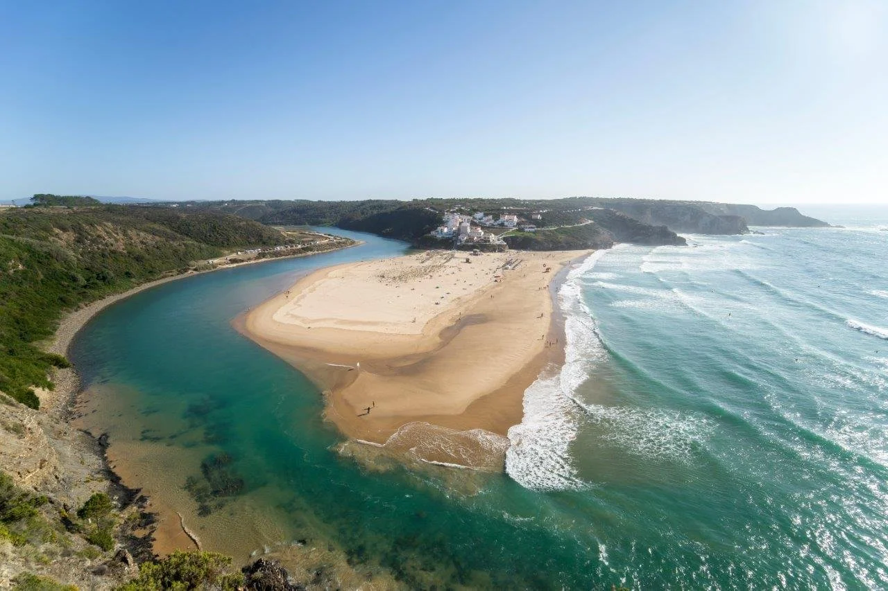Aerial view of Praia de Odeceixe where the Seixe River curves around a broad sandbar before meeting the Atlantic Ocean.