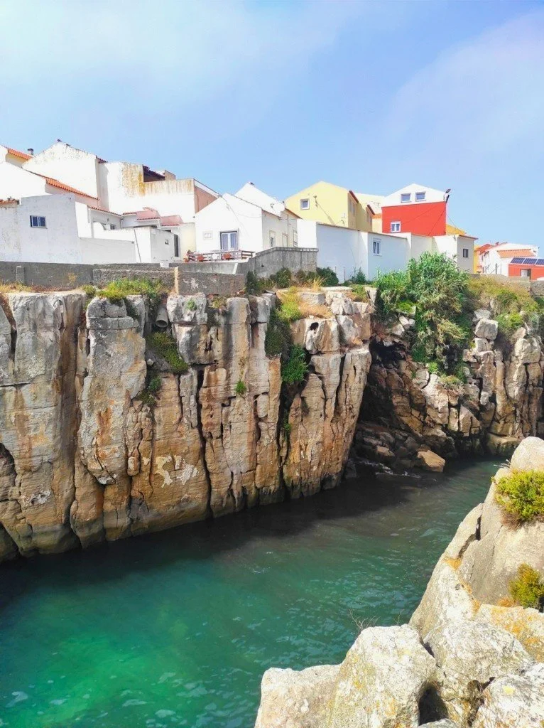 Coastal cliffs with residential buildings perched above a rocky shoreline, overlooking turquoise waters in Caldeirada de Peniche.