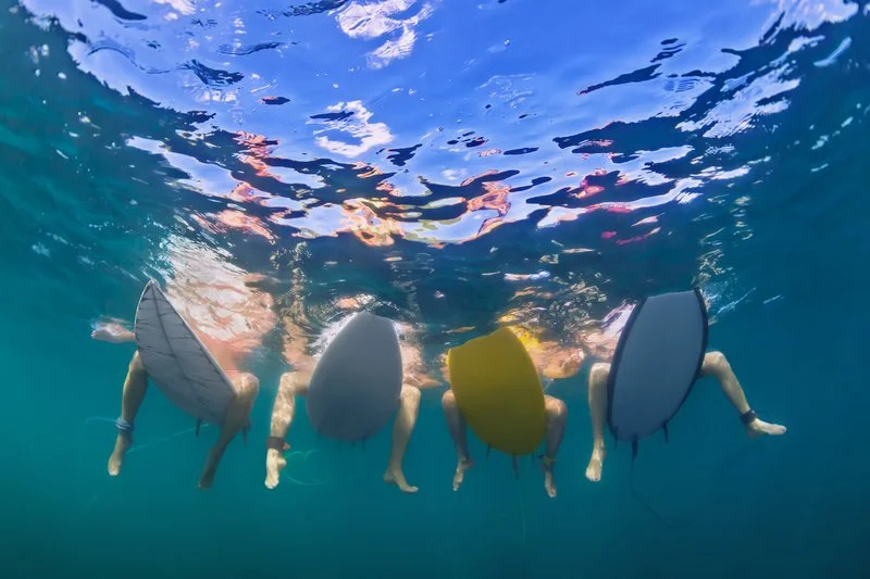 Family of four surfing on surfboards in the ocean, viewed from underneath the water, with clear blue water and waves
