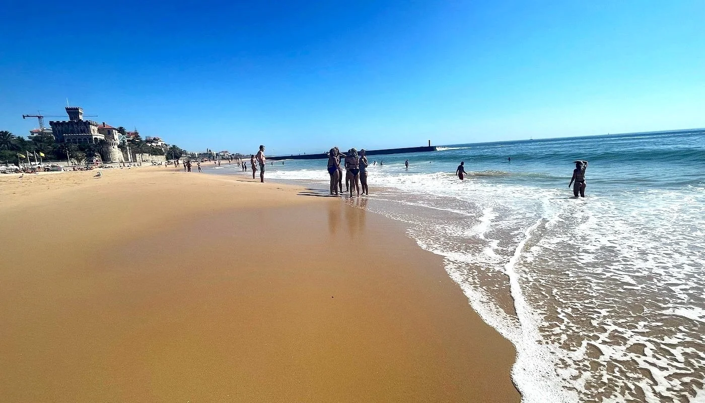 Beachgoers enjoying a sunny day on the golden sands of Praia do Tamariz (Tamariz Beach) in Estoril, Portugal, a popular destination for sunbathing, swimming, and relaxation.